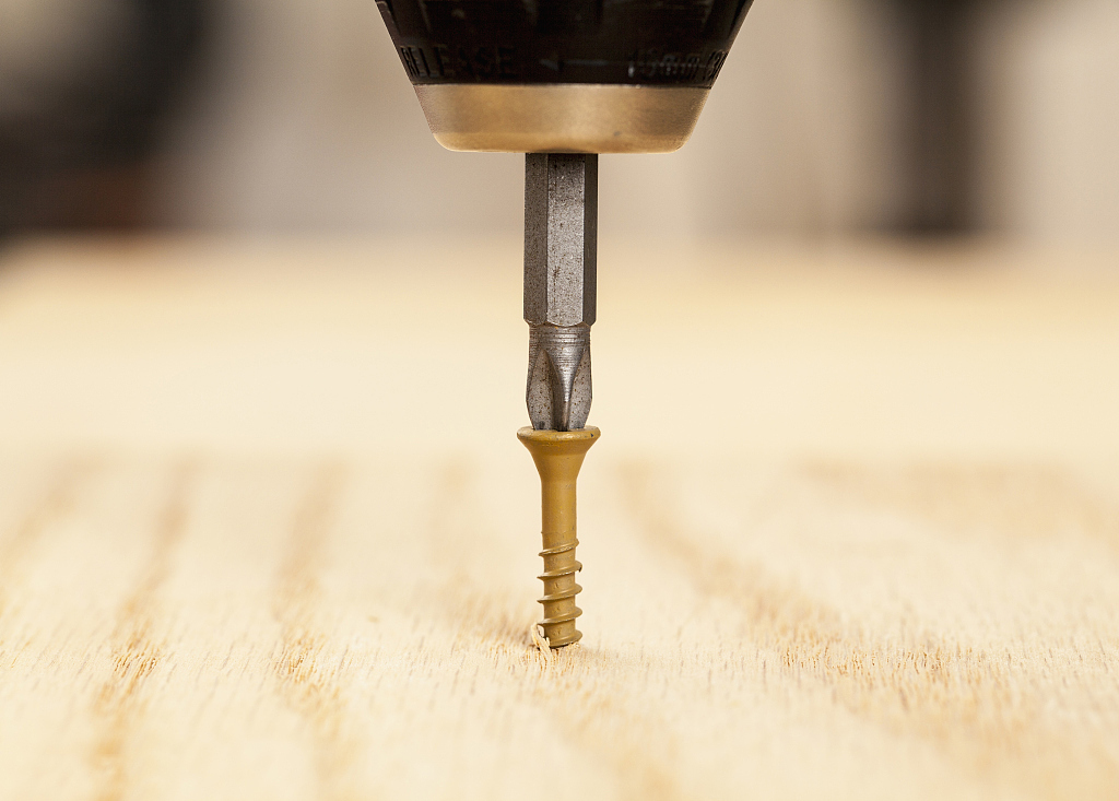 Brown screw being driven into wood by phillips bit in power drill